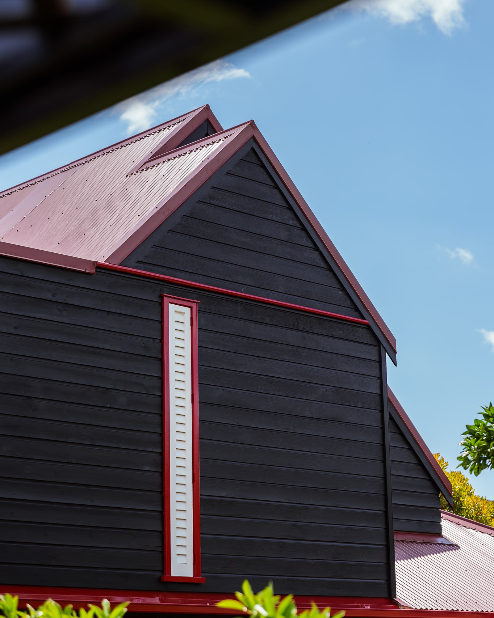 A gable end of black weatherboard with a single red vertical trim line.