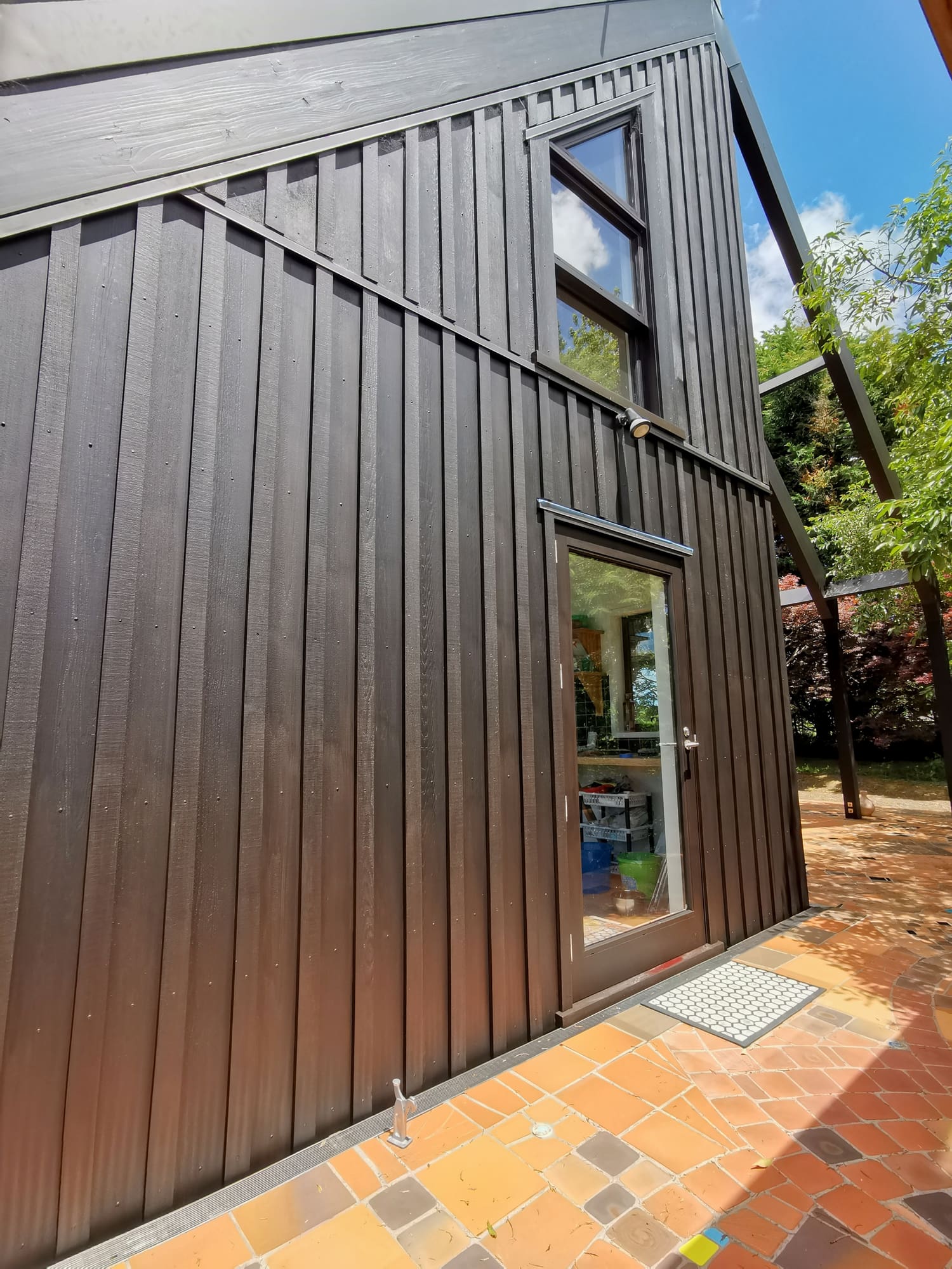 Close view of the dark brown stained vertical boards and battens beside a window.