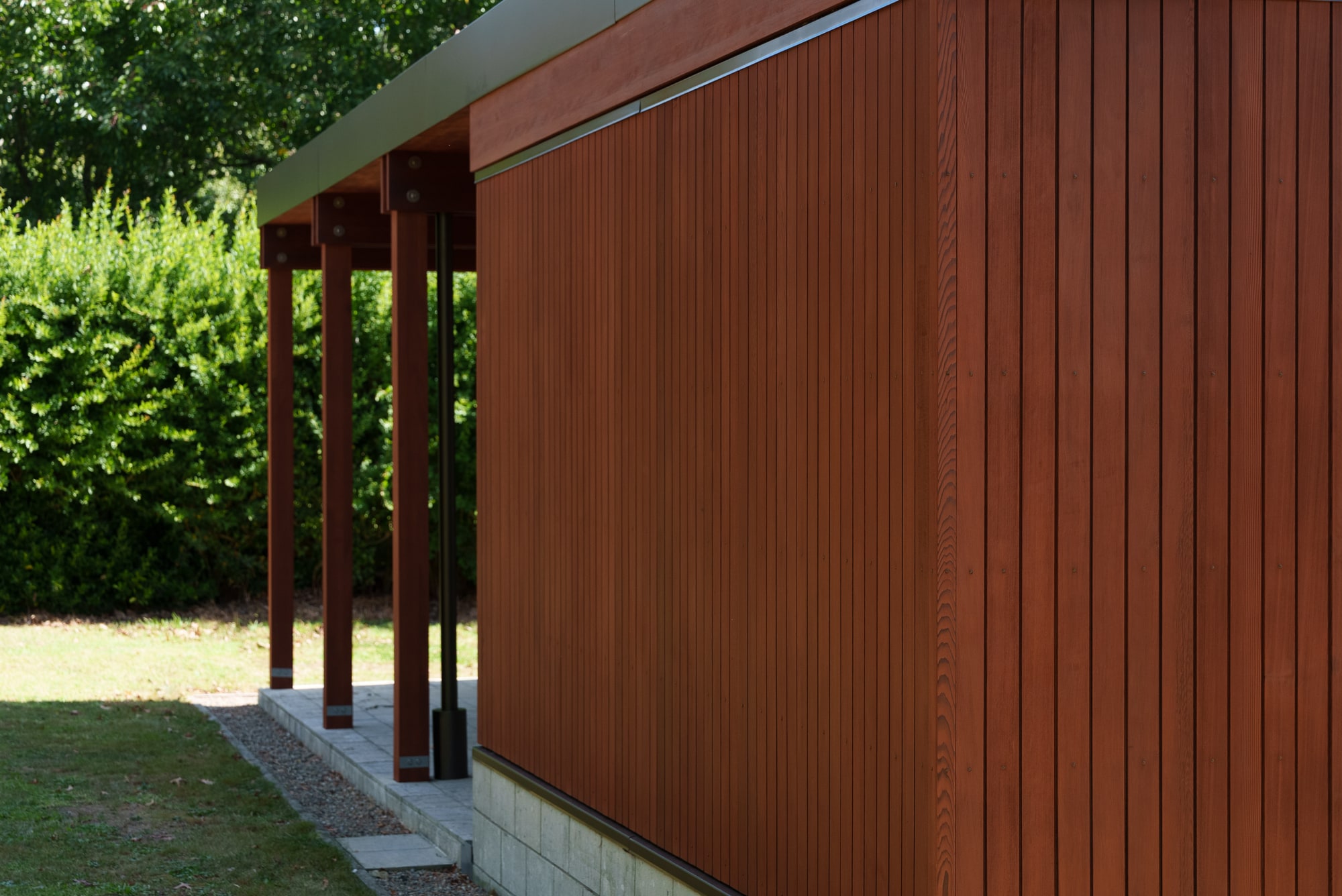 Deep reddish-brown timber cladding running past a run of posts, in full sun.