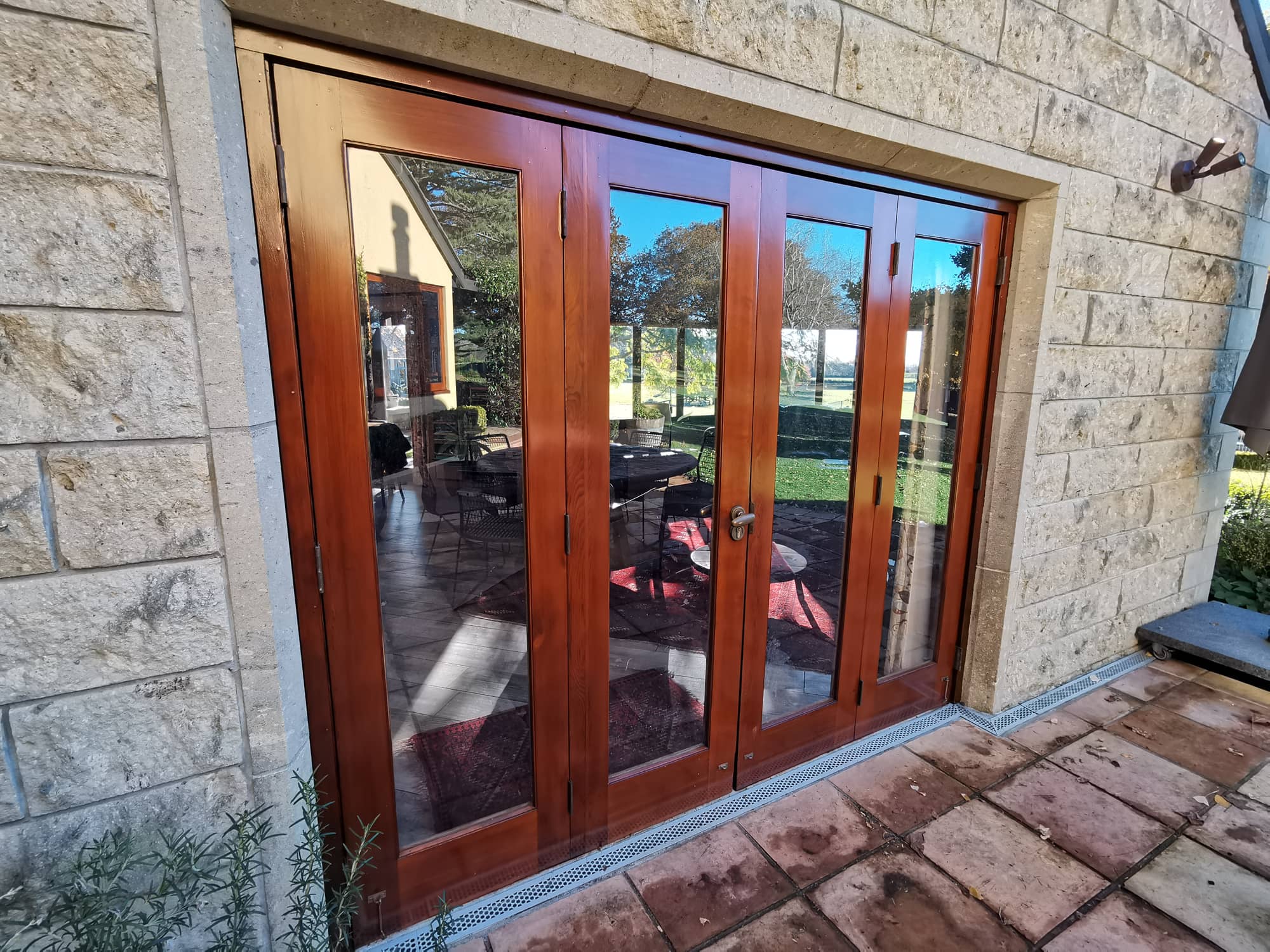 Varnished timber french doors set into a pale stone wall, opening onto a paved terrace.