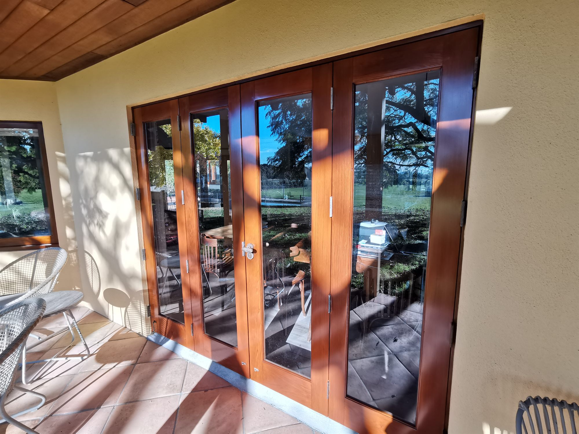 Varnished timber bifold doors opening from a tiled veranda, the garden reflected in the glass.