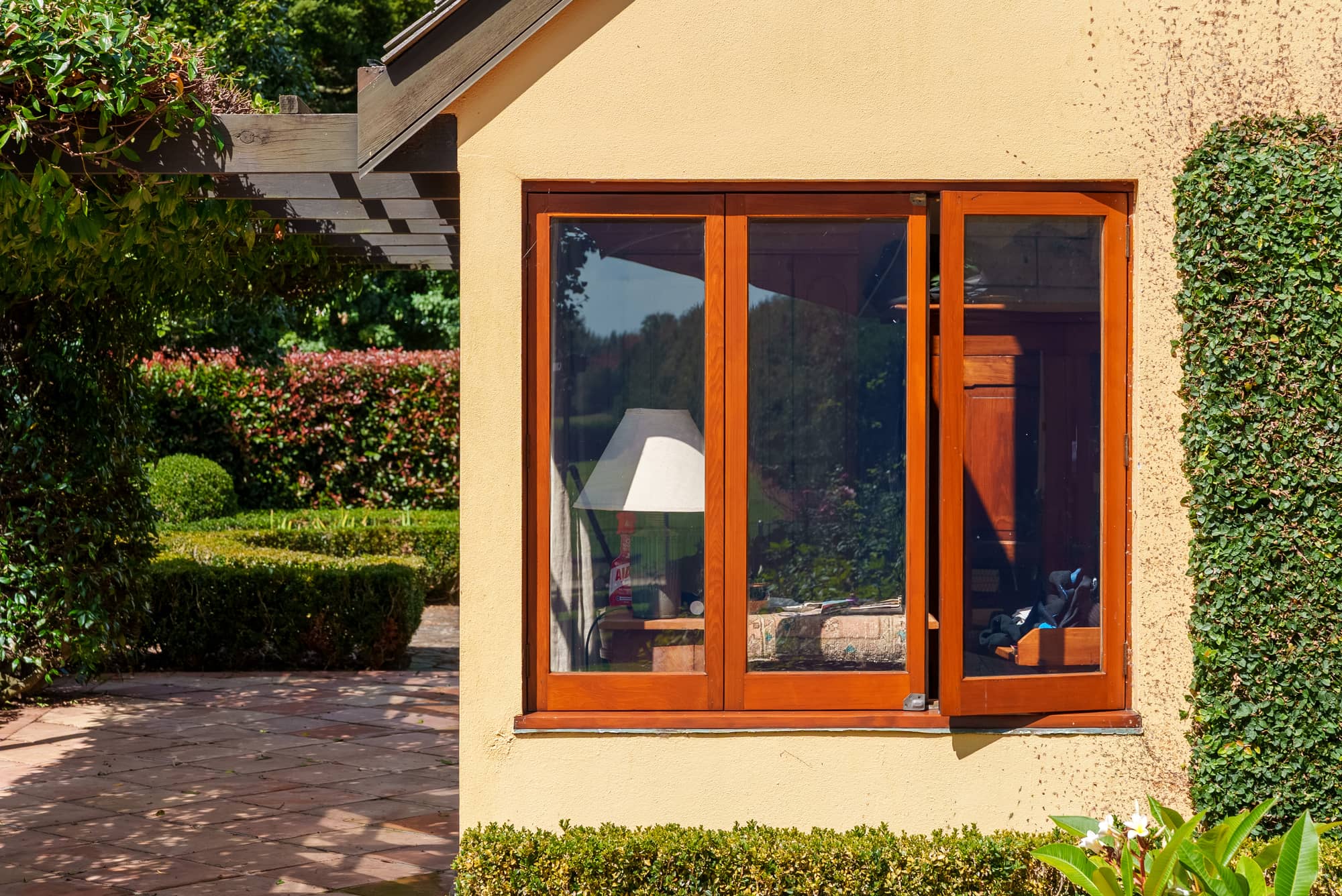 A varnished window unit above a clipped hedge.
