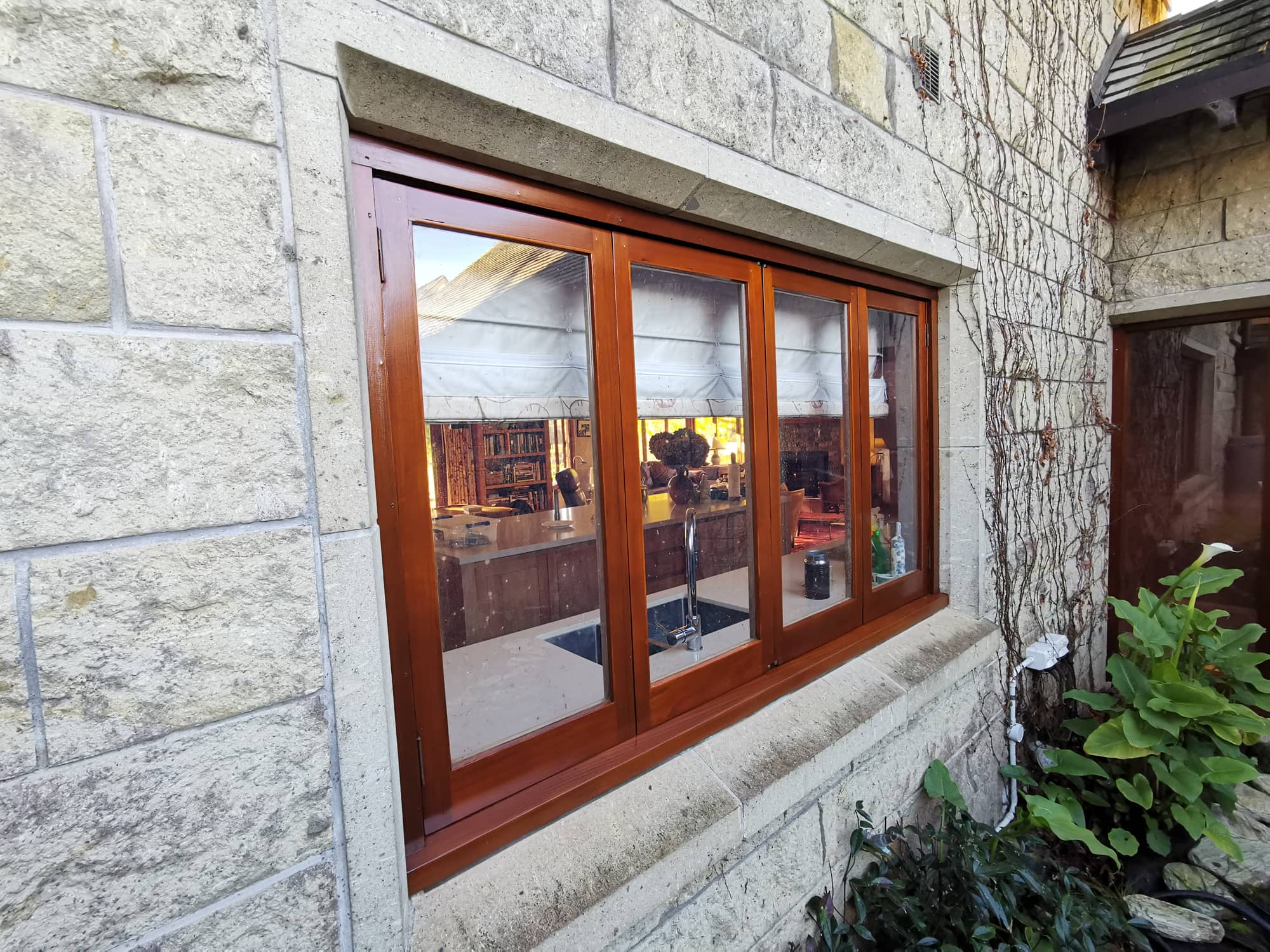 A varnished timber window in a stone wall framed by ivy.