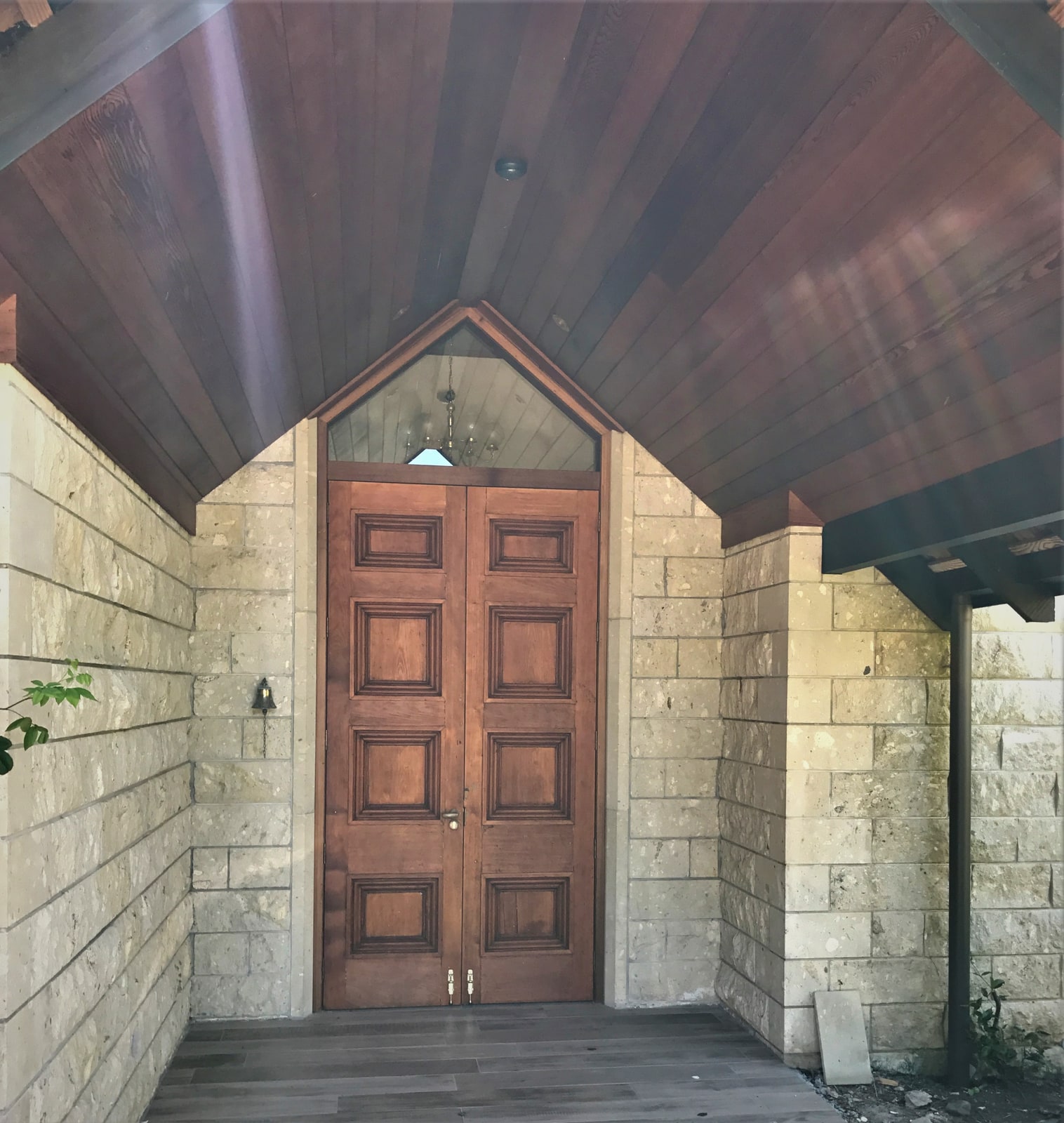 A stone entry portico with a stained tongue-and-groove ceiling and timber double doors.
