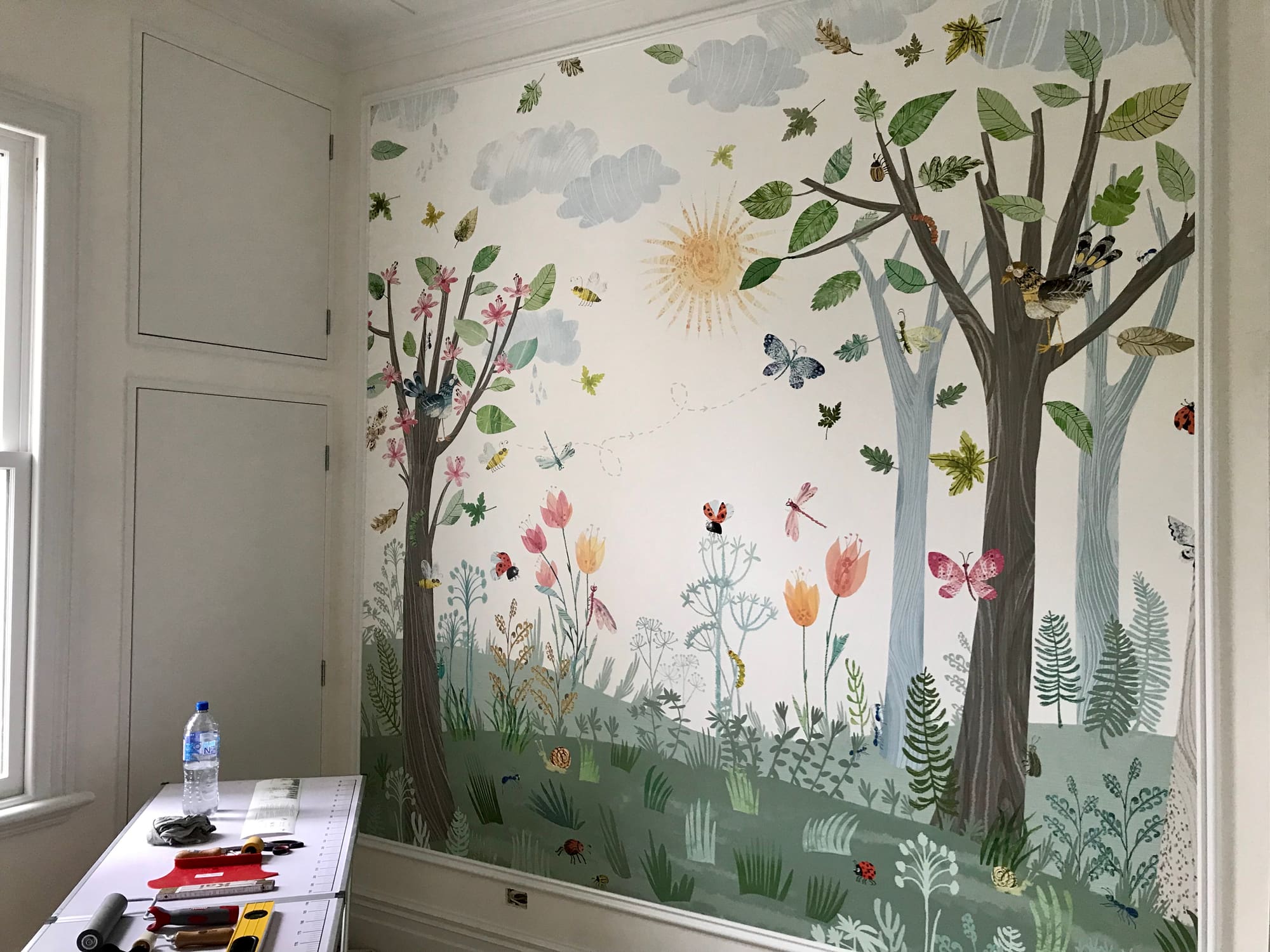 A painted forest mural wallpaper in a child's room, with trees, birds and insects.