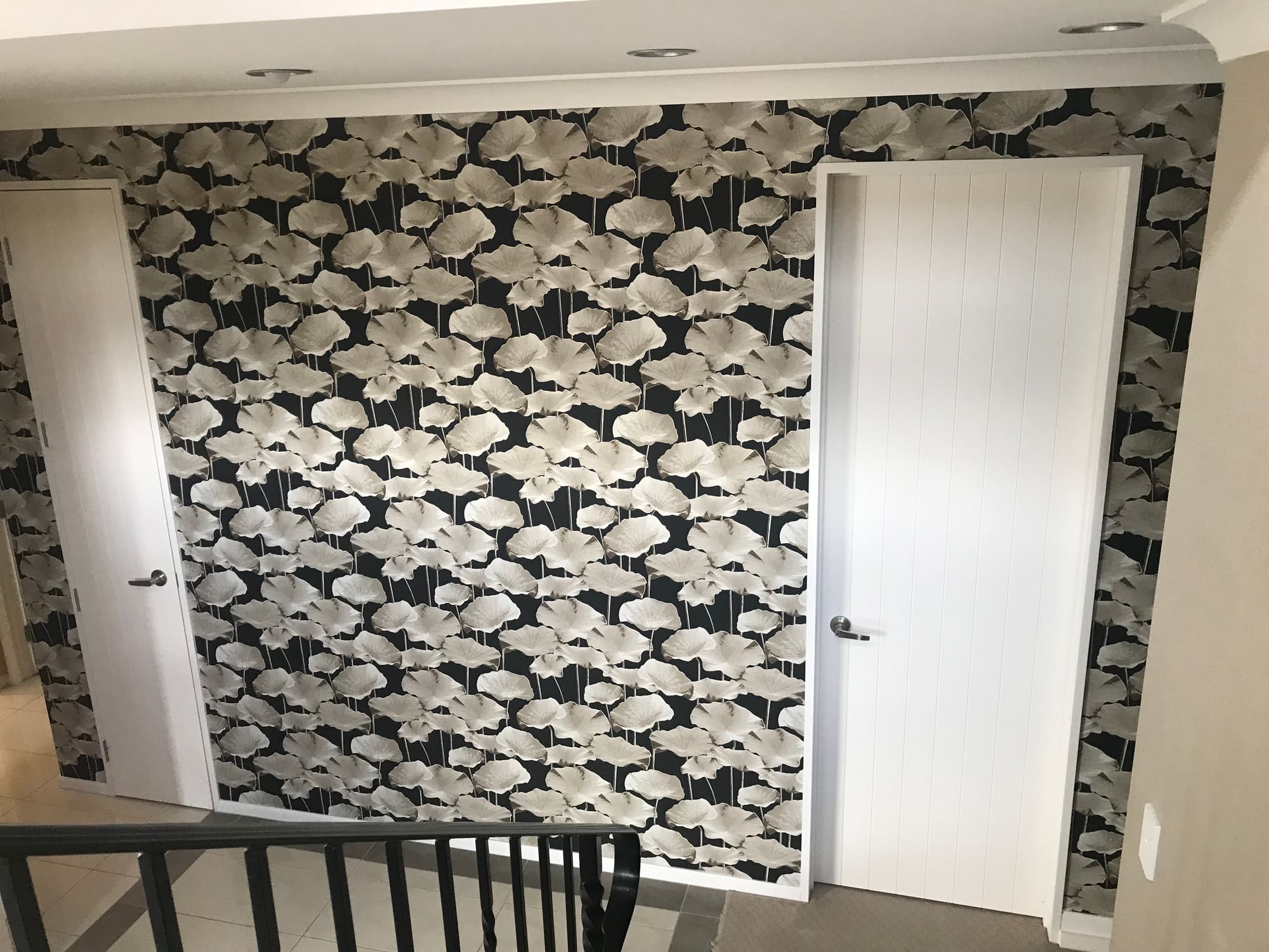 Monochrome ginkgo-leaf wallpaper on a stairwell wall between two white doors.